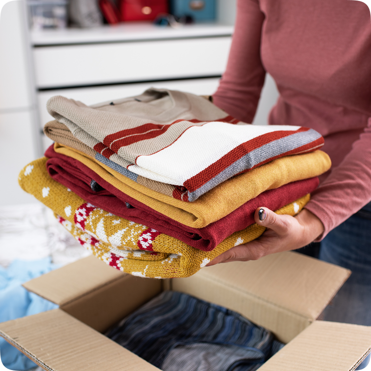 Person packing folded clothes in a box.