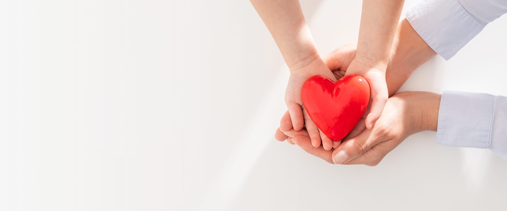 Hands holding a red heart together.